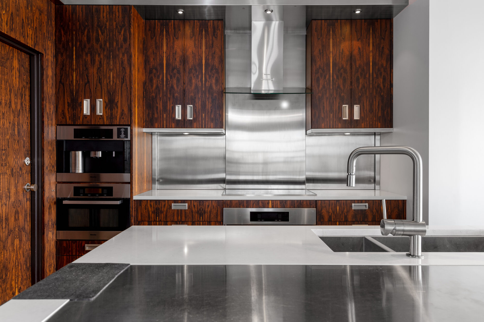 Newly remodeled kitchen featuring an eye-catching mix of dark, contemporary cabinets and gleaming stainless steel cooktop, oven, and backsplash.