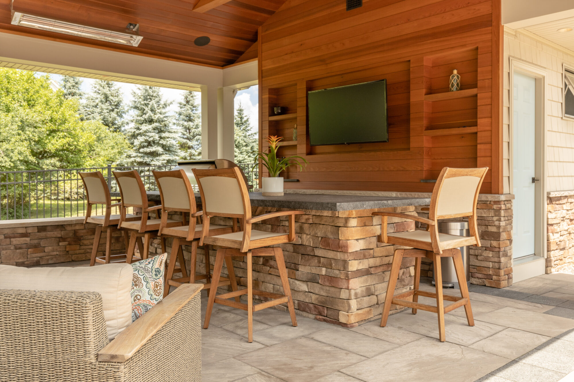 McNamara Inc's residential renovation project, displaying an outdoor patio with a cooking station, grill, minifridge, four barstools, and a TV mounted on the wall.