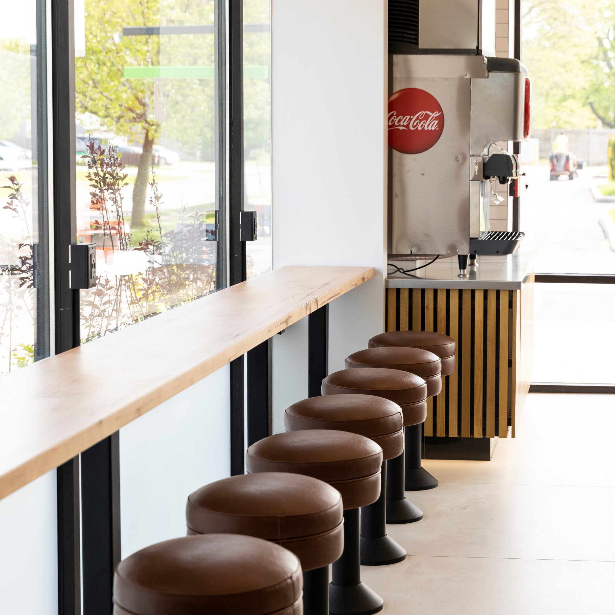 A beautifully renovated seating area at Rachel's Mediterranean Grill by R.E. McNamara Inc., featuring comfortable stool seating, light wooden accents, bright flooring, white walls, and large windows allowing ample natural light.