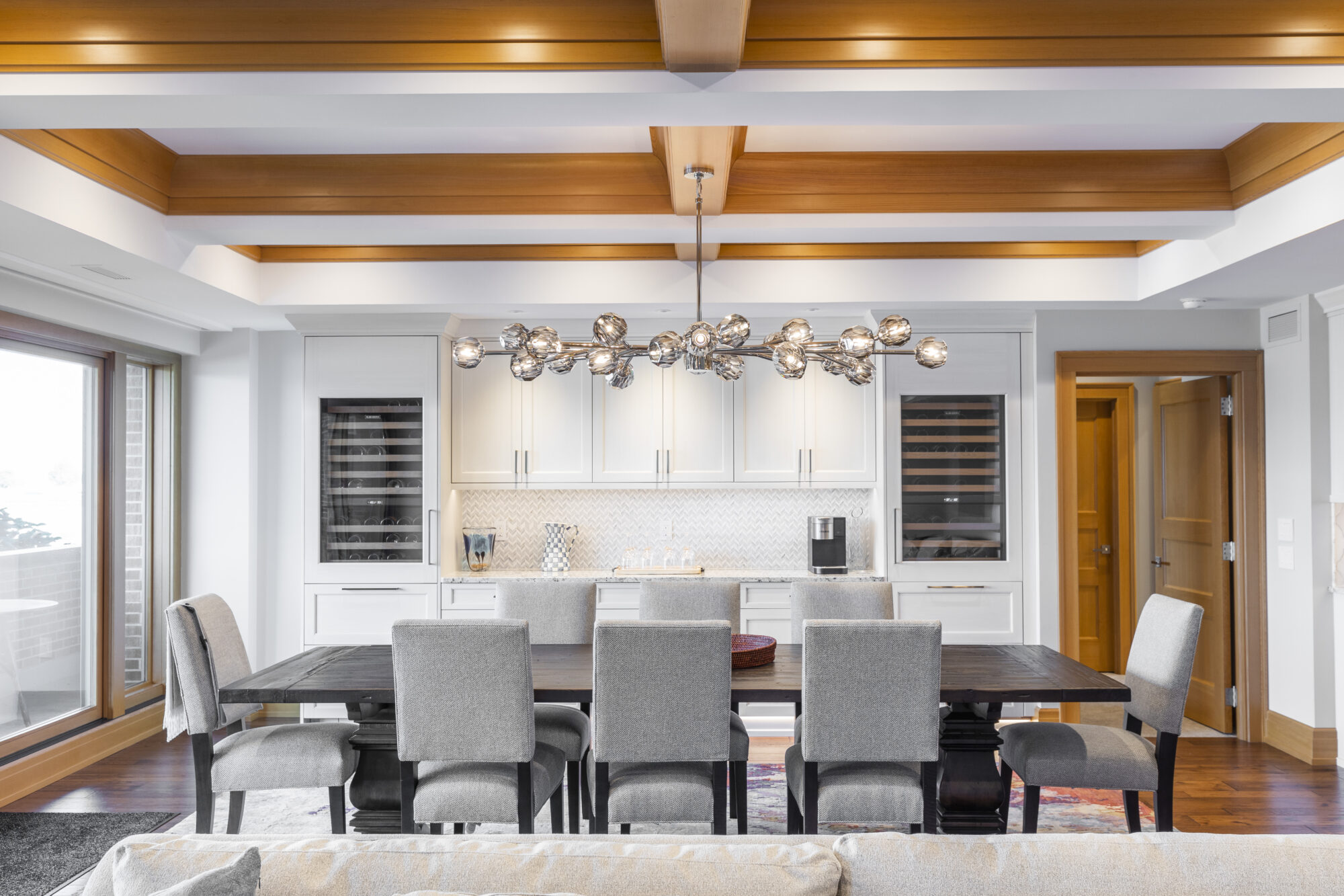 Open concept dining and living area in renovated residential space, featuring large windows, custom wooden ceiling inlay, hardwood floors, and white cabinetry by R.E. McNamara Inc.