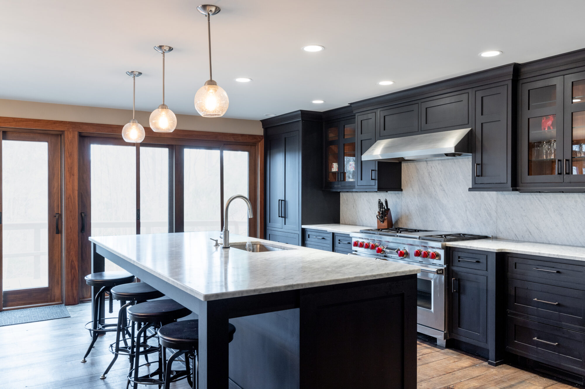 Stylish and functional kitchen in a residential renovation project, showcasing a central island with bar seating and sink, state-of-the-art two-door oven and range, rich dark custom cabinetry, and contrasting light-colored countertops, expertly designed by R.E. McNamara Inc.
