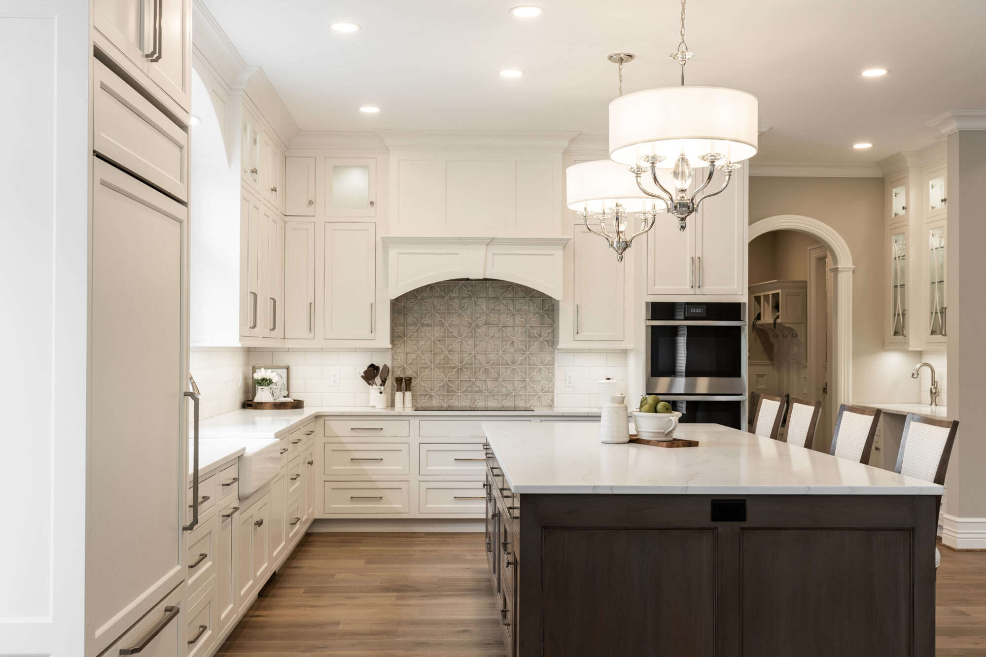 R.E. McNamara's renovated kitchen featuring light brown hardwood flooring, white custom cabinetry, and a central island with contrasting dark brown cabinets, highlighting their expertise in residential projects.
