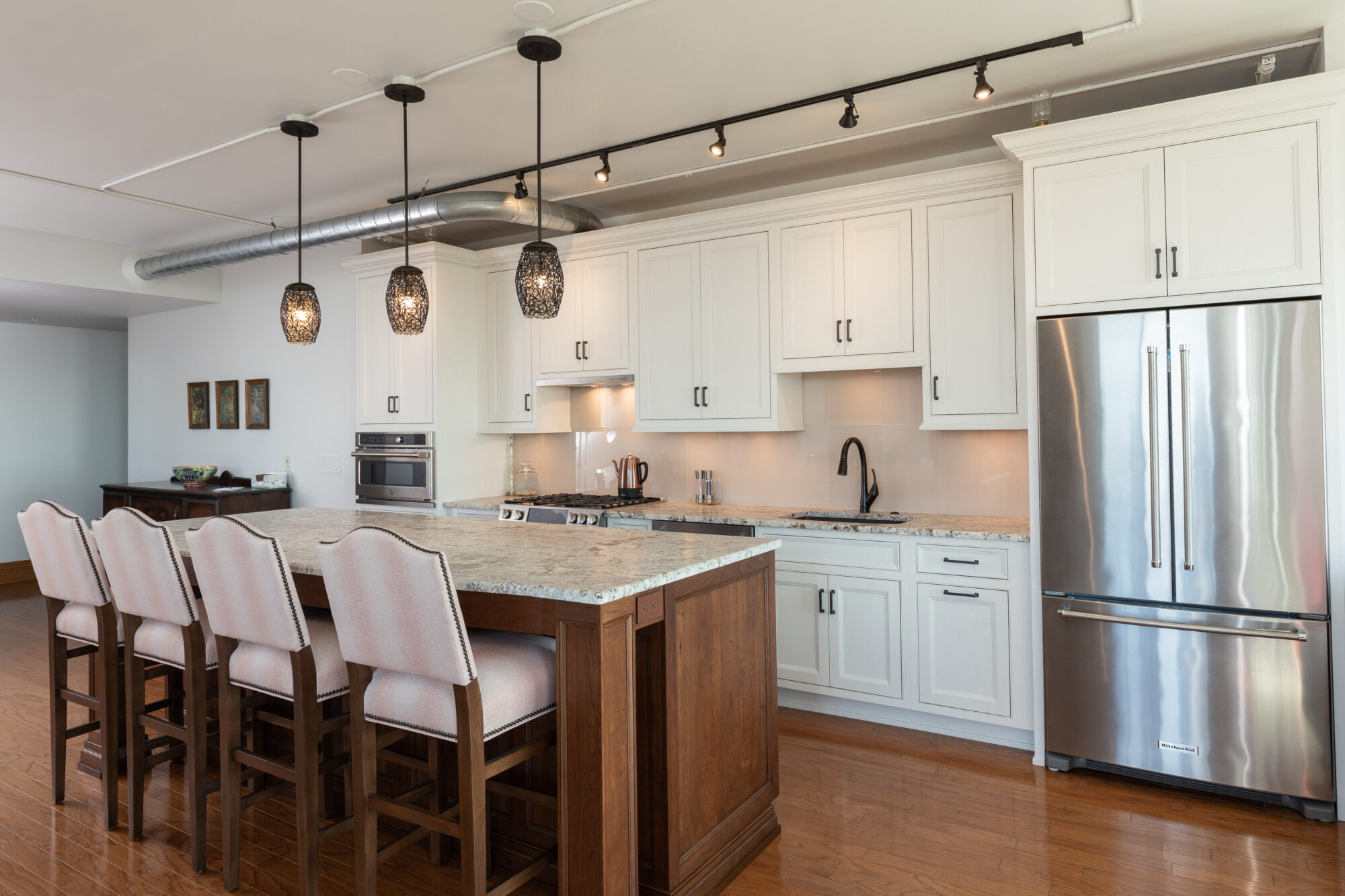Newly renovated kitchen showcasing dark wooden flooring, island with barstool seats, and white custom cabinets