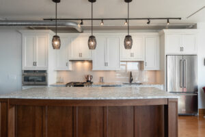 Contemporary kitchen renovation including dark wood floors, central island with barstools, and custom white cabinets