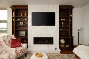 Elegant living room fireplace scene, consisting of a white tile mantle and custom dark wooden shelves on both sides, completed by R.E. McNamara Inc.