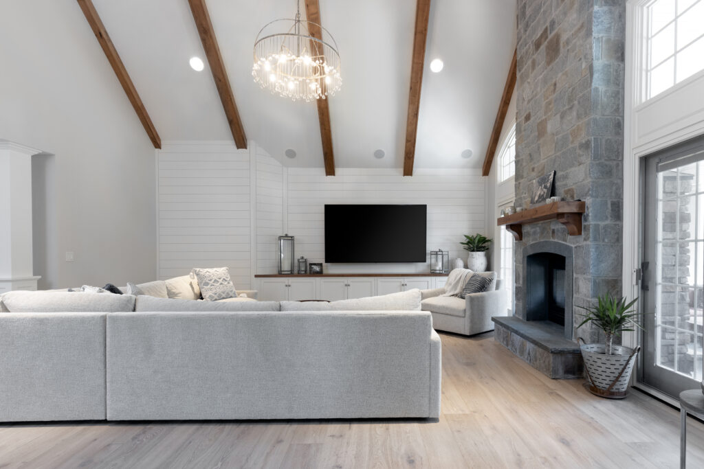 Exquisitely transformed living room by R.E. McNamara Inc. flaunting a sleek grey stone fireplace, graceful grey and white tones, hardwood floors, wooden elements, and an abundance of natural light.
