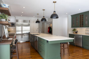 Stylish kitchen renovation, showcasing white and green cabinetry, an inviting central island with a sink and seating, a practical computer nook, and timeless hardwood flooring.