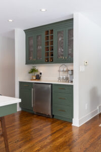 Elegant green kitchen cabinetry with integrated minifridge, wine compartments, and chic mesh cabinets
