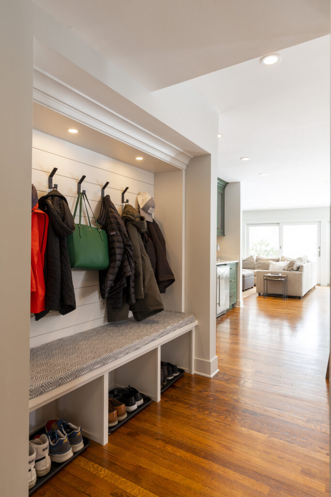 Clothing nook with hooks, built-in wooden bench with shoe storage, and sophisticated wooden details by R.E. McNamara Inc.