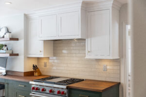 Detail of white overhead cabinetry, matching backsplash, and leek wooden countertops.