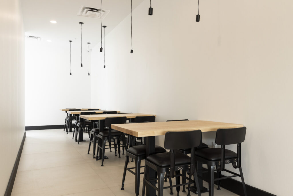 Renovated seating area at Rachel's Mediterranean Grill by R.E. McNamara Inc. featuring four tables with black chairs, light wooden accents, bright flooring, and white walls. Accessible and modern commercial design.