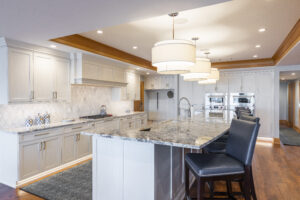 Kitchen renovation by R.E. McNamara, showcasing white bespoke cabinets, granite worktops, wooden details, a chic backsplash, and a dual-level island with sink and bar seating area