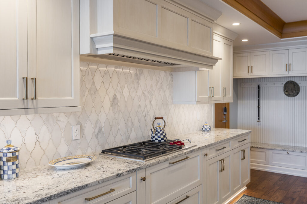 Renovated kitchen with white cabinets, granite countertops, wooden accents, elegant backsplash, and a two-level island with a sink and bar seating
