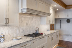 Renovated kitchen with white cabinets, granite countertops, wooden accents, elegant backsplash, and a two-level island with a sink and bar seating
