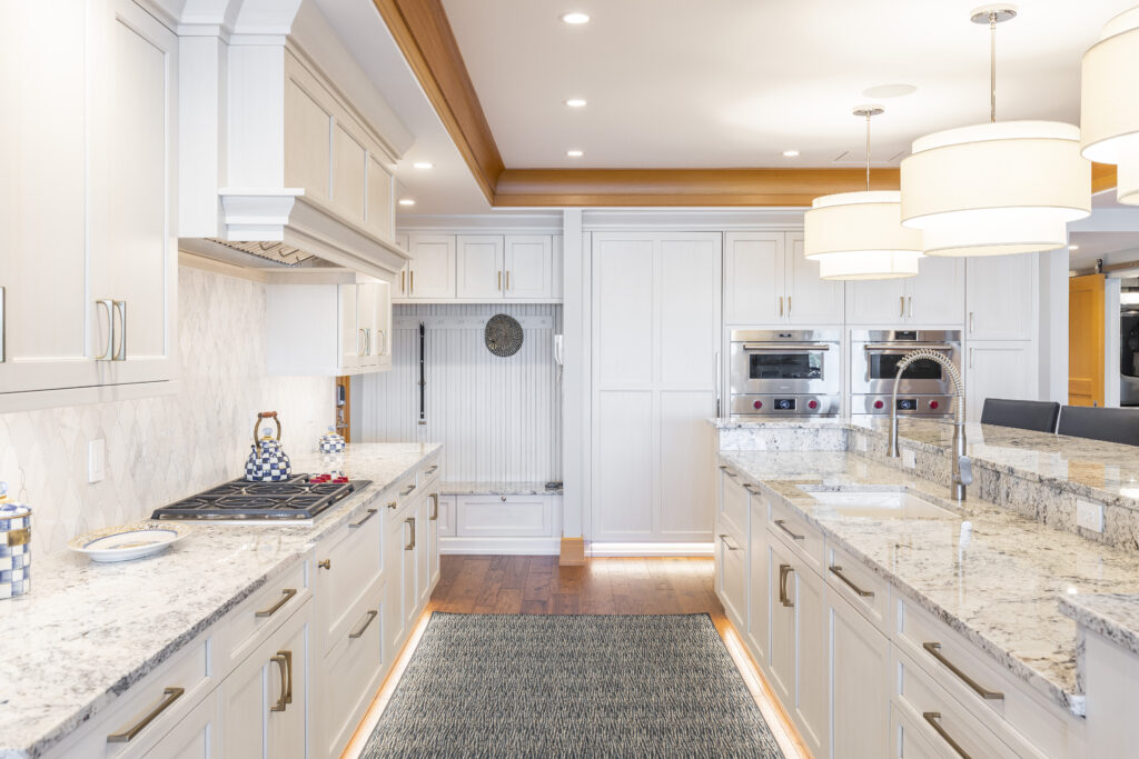 R.E. McNamara-renovated kitchen featuring white custom cabinetry, granite counters, wood highlights, stylish backsplash, and a multi-level island with sink and barstools