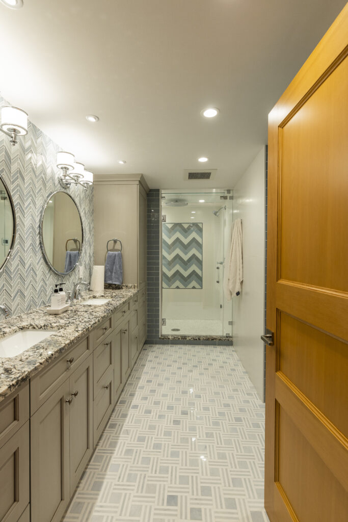 Elegant renovated bathroom by R.E. McNamara Inc., featuring blue and white tones, tiled flooring, herringbone backsplash, his and hers sinks, and walk-in shower.