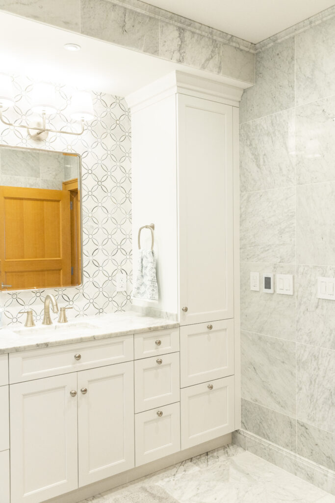 Renovated bathroom by R.E. McNamara showcasing his and hers sinks, elegant backsplash, marble tiling on the floor and walls, and ample cabinetry space for a luxurious residential project.
