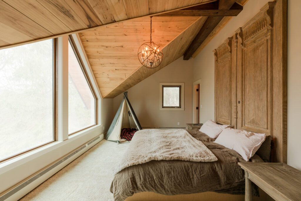 A spacious and well-lit bedroom with sunlight pouring in through large windows, showcasing a stylish custom headboard with a mix of beige and warm brown tones, creating an inviting and cozy atmosphere