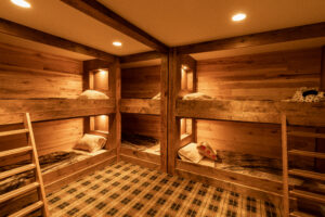 Bunk beds surrounded by rich, dark wood paneling, with each bunk adorned with its own softly illuminated shelf