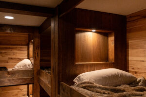 Warm and cozy bunk lodging with dark custom woodwork, decorative paneling, and a softly lit shelf above each bunk, showcasing R.E. McNamara Inc.'s residential renovation expertise.