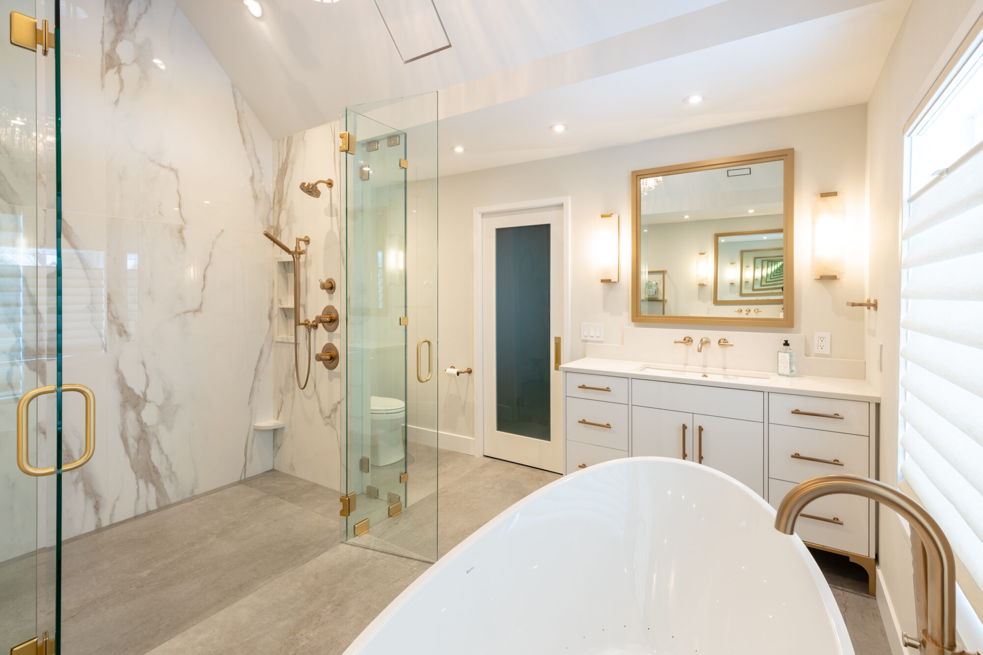 Beautiful bathroom remodel by R.E. McNamara Inc. showcasing an off-white palette, walk-in glass shower, freestanding tub, and sink setup