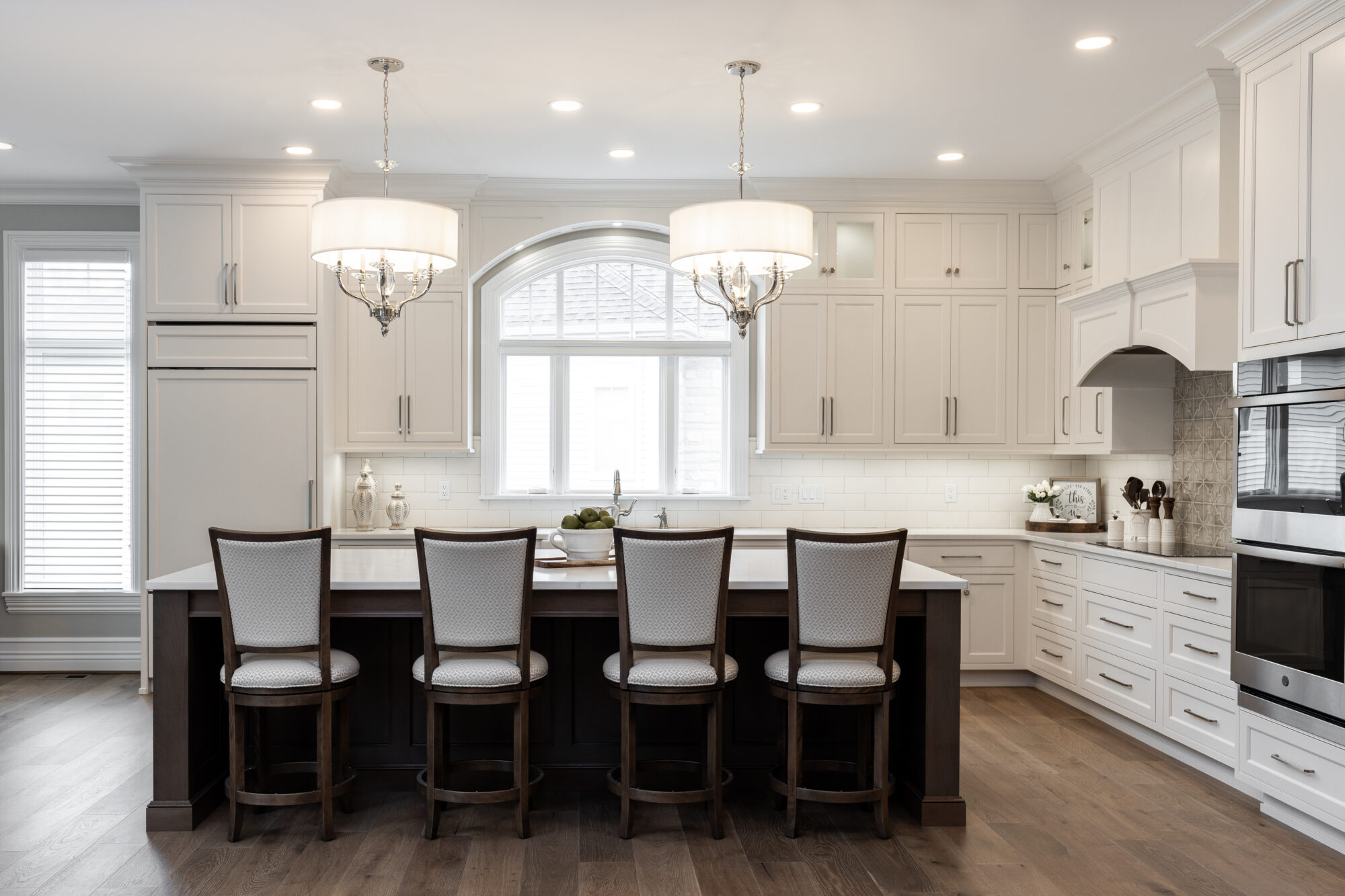 A beautifully renovated kitchen featuring light brown hardwood flooring, white custom cabinetry, and a central island with contrasting dark brown cabinets.