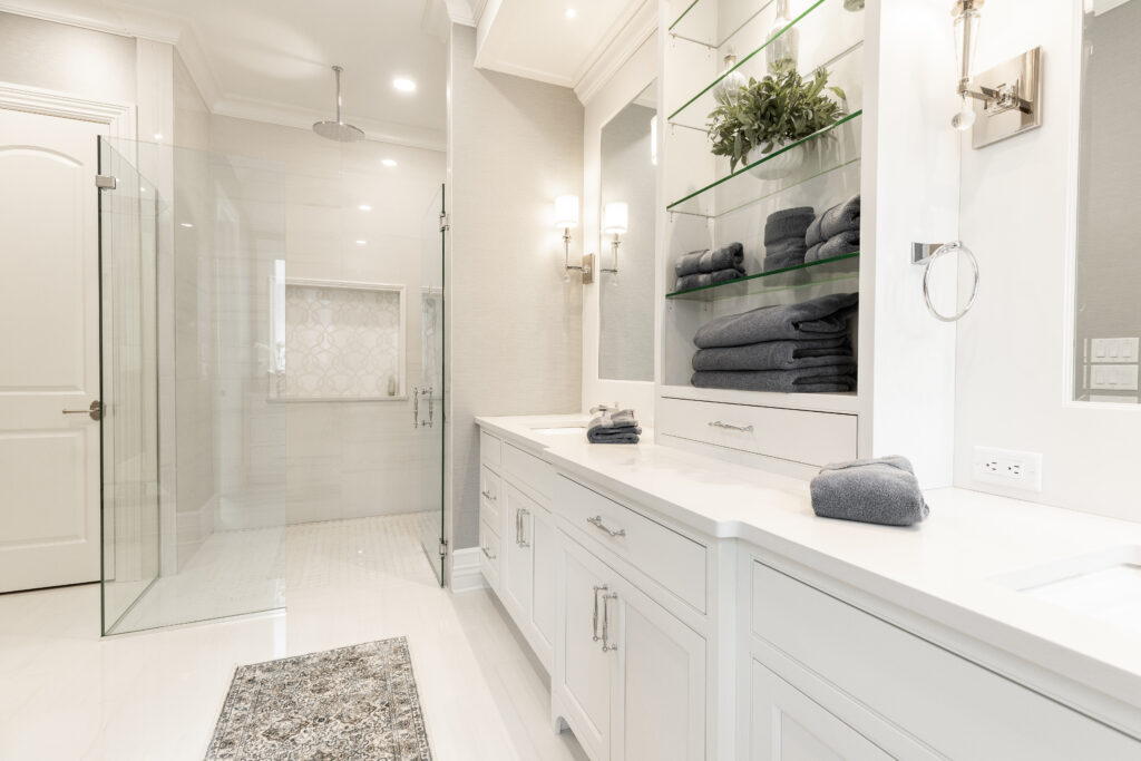 functional renovated residential bathroom, featuring his and hers sinks with white cabinetry, sleek glass shelving, and a spacious walk-in shower