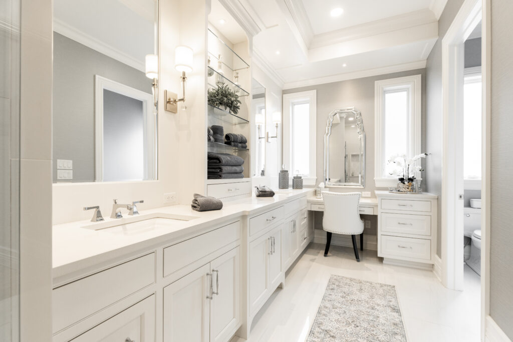 A beautifully renovated bathroom showcasing his and hers sinks with sleek white cabinetry, elegant glass shelving, and a custom-made vanity, reflecting our 45 years of experience in residential projects