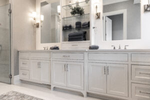 A beautifully renovated bathroom featuring his and hers sinks, white cabinetry, and elegant glass shelving