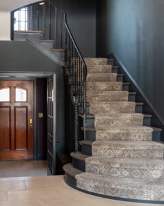 A stunning renovated entryway in a residential property, showcasing a dark-colored staircase set against elegant dark walls.