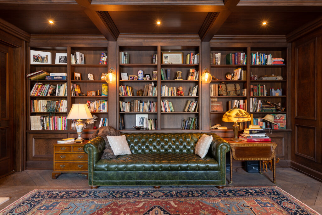 A stunning study room in a residential renovation project by R.E. McNamara Inc., featuring custom-made dark wood shelving filled with books, elegant ceiling accents, and a cozy central sofa that invites you to delve into a good read.