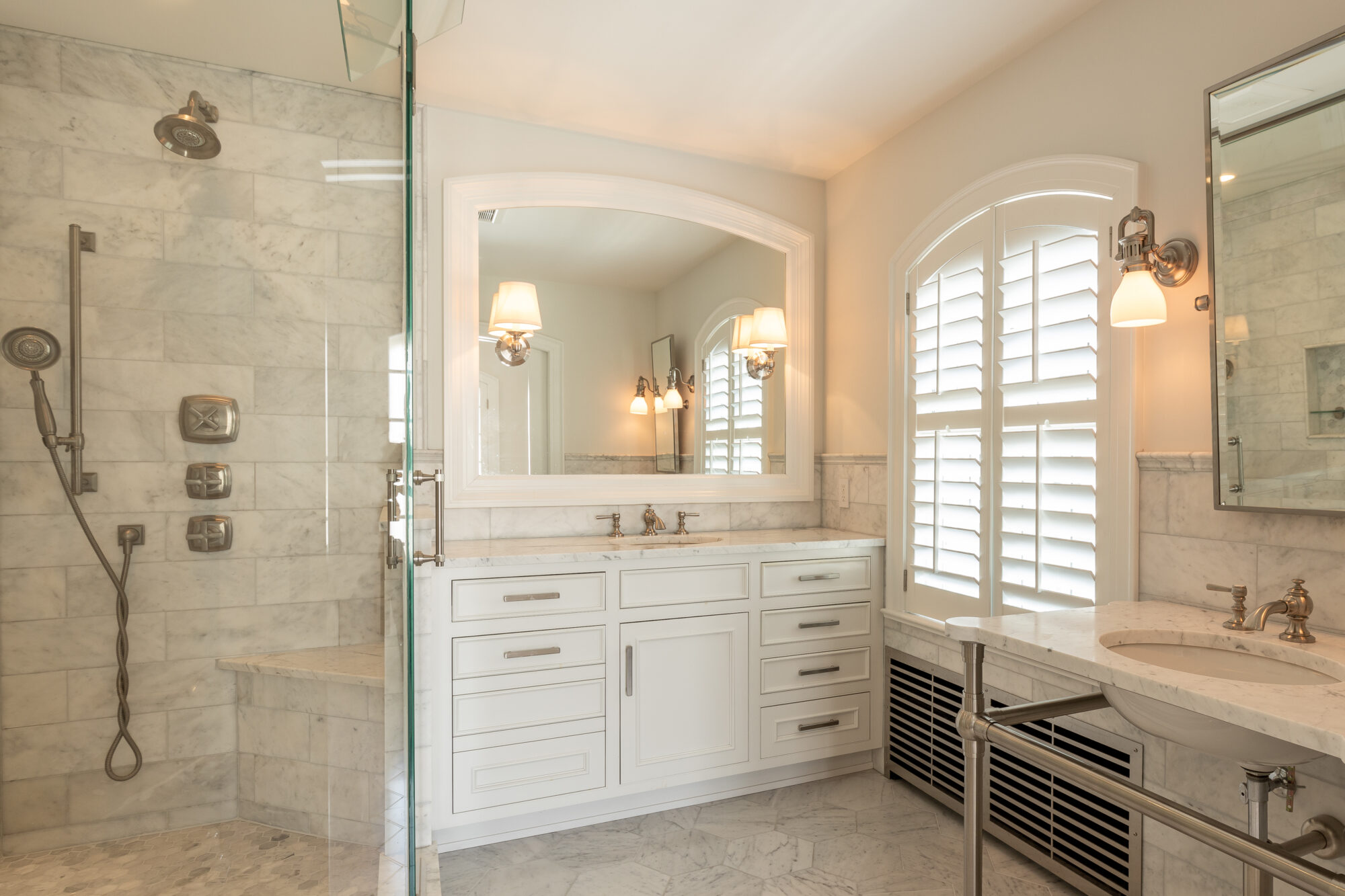 Refined bathroom transformation by R.E. McNamara Inc., showcasing a stylish walk-in shower with a transparent glass door, crisp white cabinetry, sophisticated marble tiles, and tasteful modern accents.