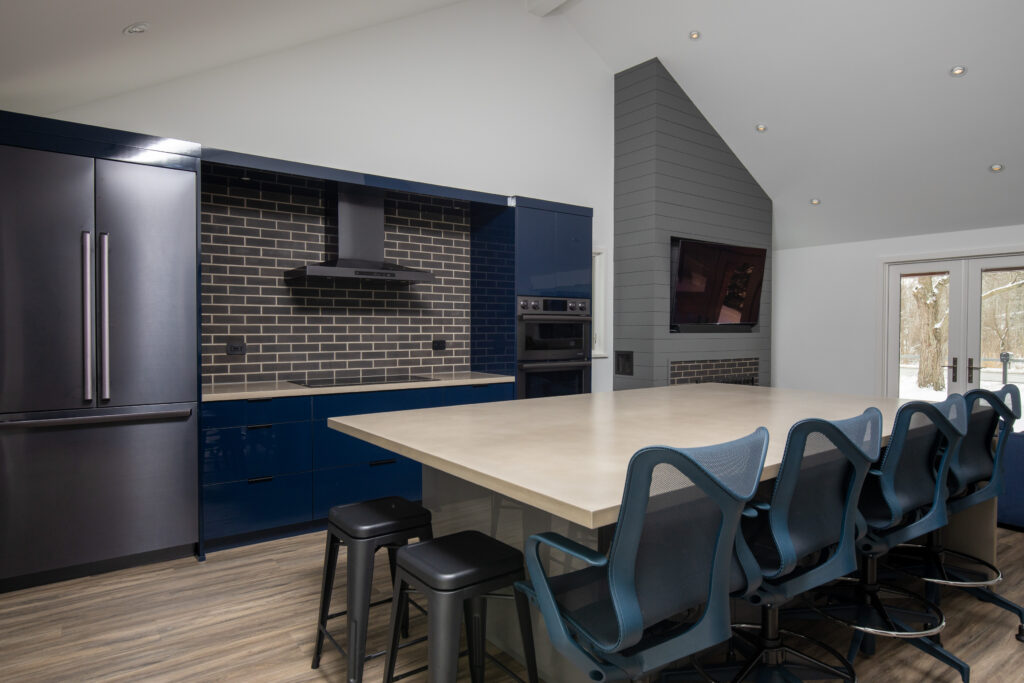 Modern kitchen and living area with navy blue cabinets, light grey wood paneling, white walls, and a spacious island
