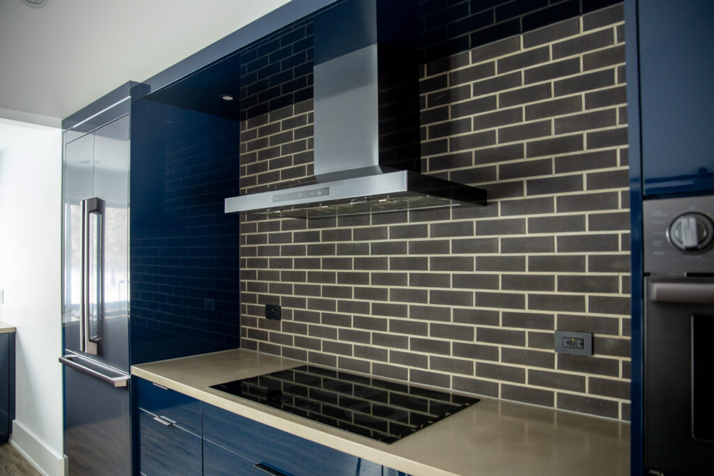 kitchen showcasing navy blue cabinetry, light-colored countertops, and a contrasting dark tiled backsplash