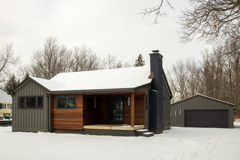 Snow-covered house displaying unique custom wood paneling and dark vertical siding, a testament to our comprehensive general contracting services