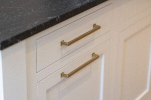 Detail of a gold colored handle on white colored cabinets
