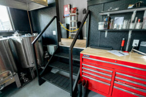R.E. McNamara Inc. renovated One Eyed Cat Brewing workspace featuring workbench, metal staircase, and brewing equipment.