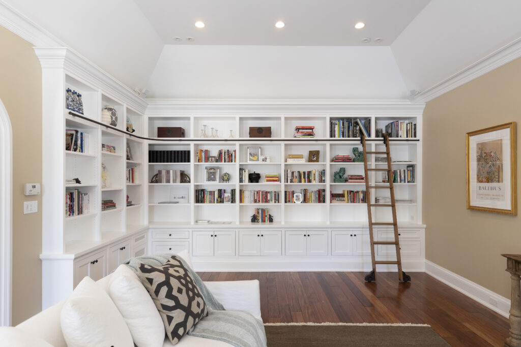 Elegant white cabinetry adorns a custom bookcase wall in a beautifully renovated residential space by R.E. McNamara Inc. Serene and inviting ambiance is accentuated by the neatly arranged books and decorative items