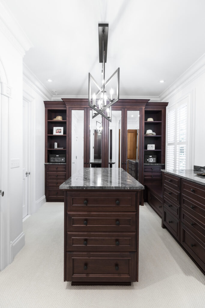Luxurious walk-in closet with pristine white walls and rich dark brown shelving, featuring a central island for stylish shoe storage, showcasing R.E. McNamara Inc.'s impeccable residential renovation expertise.