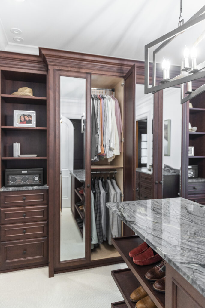 A stunning walk-in closet renovation features pristine white walls and rich, dark brown shelving units, including a central island dedicated to shoe storage.