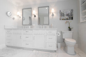 Elegant bathroom renovation featuring white tiled walls and floors, dual white cabinets, and his & hers sinks