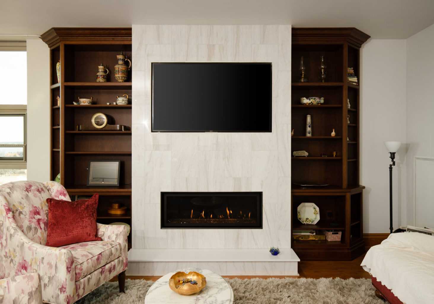 Elegant living room fireplace scene, consisting of a white tile mantle and custom dark wooden shelves on both sides, completed by R.E. McNamara Inc.