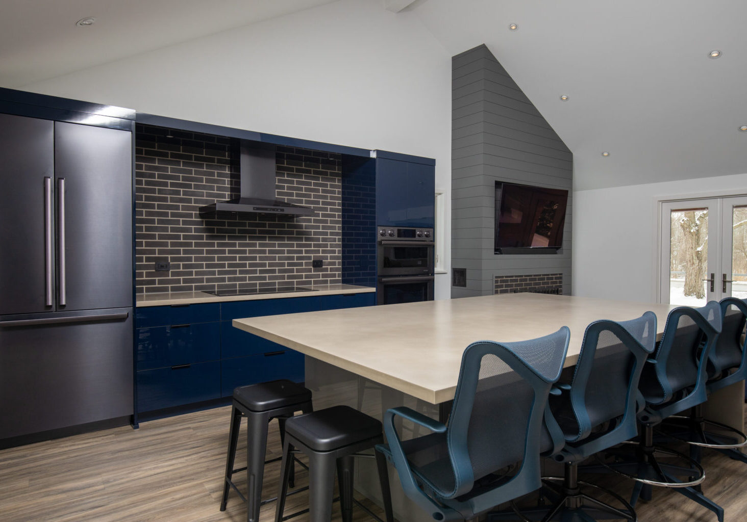 Modern kitchen and living area with navy blue cabinets, light grey wood paneling, white walls, and a spacious island